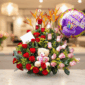 Arreglo de flores con rosas rojas y rosas, flores exóticas naranjas, peluche de oso y globo de feliz cumpleaños sobre mesa en interior