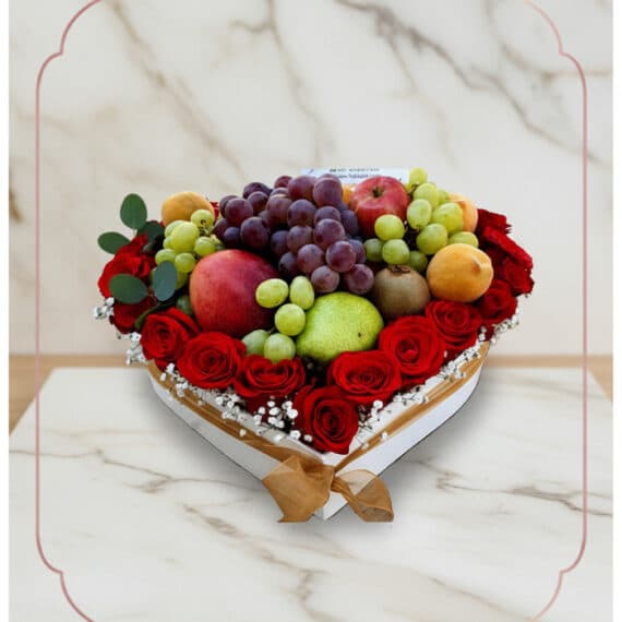Arreglo floral ARMANI con frutas frescas variadas y rosas rojas dispuestas en una caja blanca en forma de corazón, ideal para