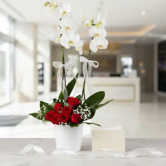 Arreglo floral BRIANA con orquídeas blancas y rosas rojas, tarjeta de regalo y cinta satinada en un elegante lobby.