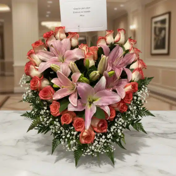 Arreglo floral Feliz Contigo con lirios rosados y rosas bicolor sobre mesa de mármol, fondo elegante de lobby de hotel boutiq