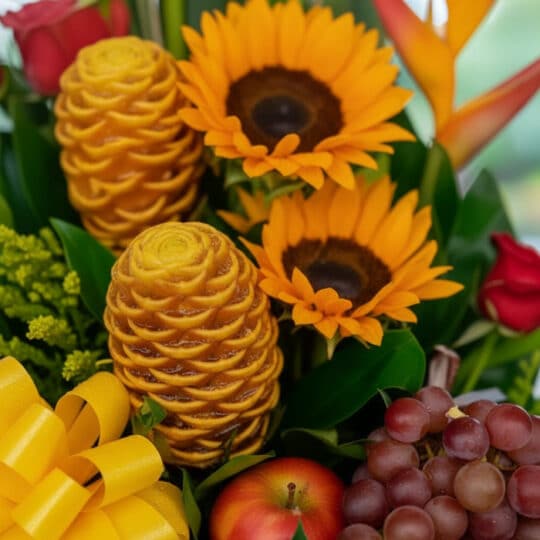 Primer plano extremo de un arreglo floral con frutas Durio, girasoles, rosas rojas, uvas y una manzana, destacando texturas y