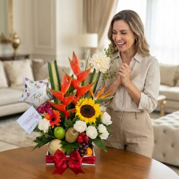 Mujer elegante sonriendo y admirando un arreglo floral con frutas tropicales, girasoles, rosas y aves del paraíso, en un lujo