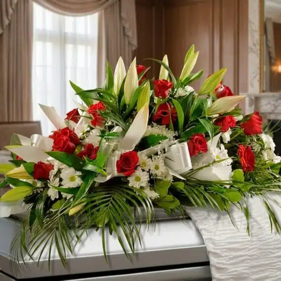 Elegante Arreglo Fúnebre Cubre Caja Paraíso con Rosas y Lirios Arreglo fúnebre cubre caja Paraíso con rosas rojas, lirios blancos y margaritas, sobre un ataúd en una sala de velación premi