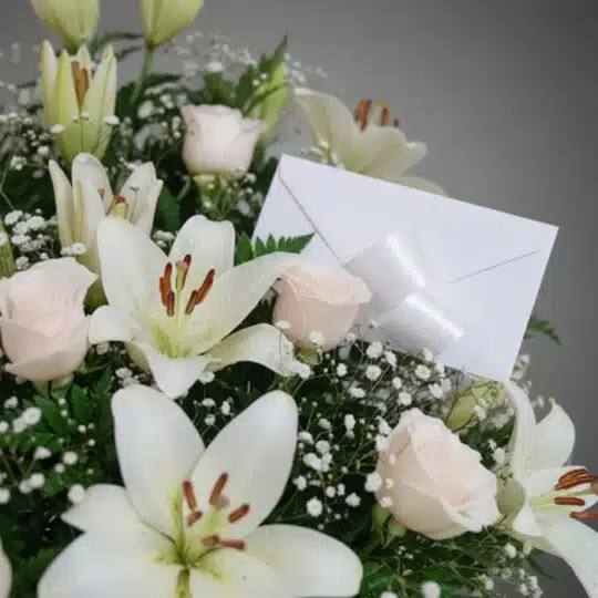 Fotografía macro premium del Arreglo Fúnebre Infinito con lirios blancos, rosas pálidas y follaje verde, con rocío sutil y ci