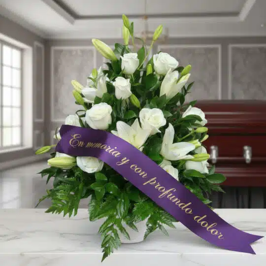 Arreglo fúnebre Piedad con rosas y lirios blancos, cinta morada con mensaje de condolencia, en sala de velación premium.
