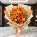 Bouquet LIRICA con lirios naranjas vibrantes, rosas amarillas abiertas y gerberas rojas, envuelto en papel coreano elegante s