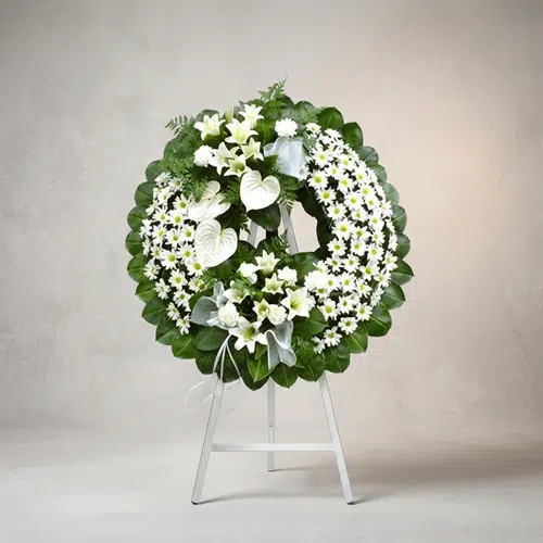 Corona Fúnebre Legado de Paz: Homenaje Floral Elegante y Sereno Corona fúnebre Legado de Paz con flores blancas, lirios, margaritas y anturios, sobre un caballete blanco en un fondo elegant