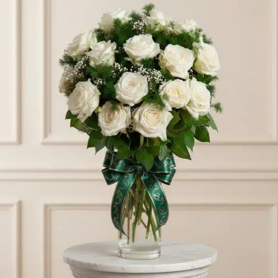 Jarrón Pétalos Blancos: Elegante Arreglo Floral con Rosas y Verdes Jarrón Pétalos Blancos con un arreglo floral de rosas blancas abiertas, follaje verde y un moño verde elegante, sobre una sup