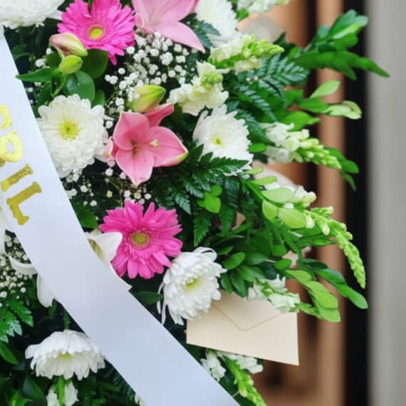 Fotografía macro premium de un arreglo fúnebre Pedestal Sagrado con flores blancas, rosas y follaje verde, rocío sutil, cinta