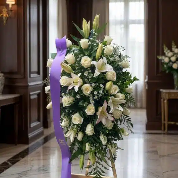 Pedestal fúnebre Salvación con rosas blancas, lirios y follaje verde, presentado en una sala de velación premium con luz natu